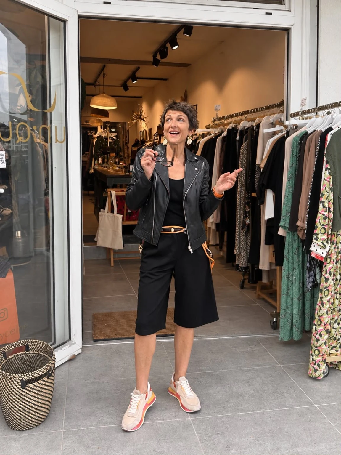 Céline souriante à l’entrée de sa boutique, en veste noire et baskets