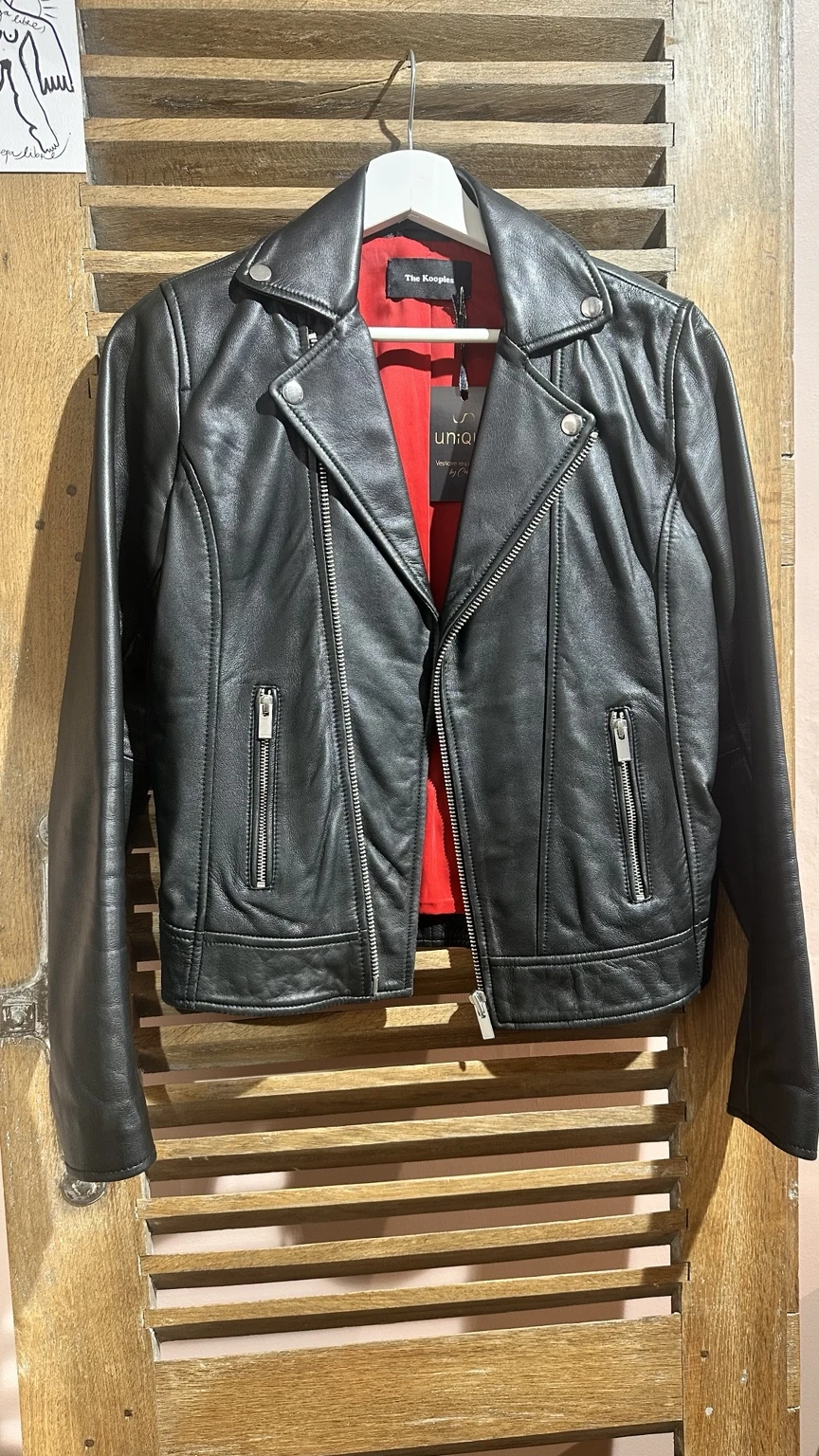 Perfecto noir en cuir, doublure rouge, présenté sur un portant en bois